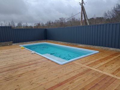 Голубой прямоугольный композитный бассейн на деревянной площадке, огражденный профлистом